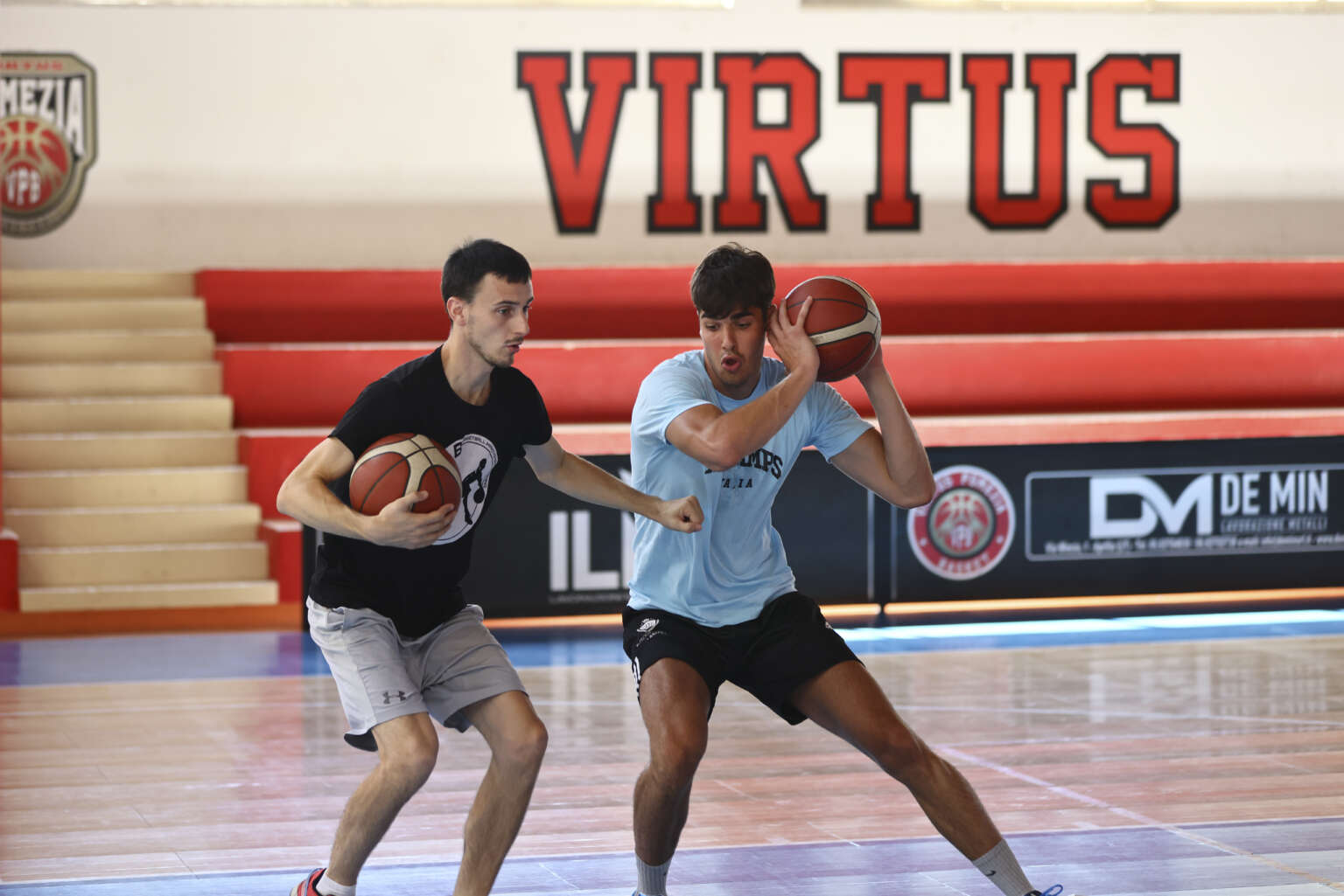 Due atleti si allenano con palloni da basket, uno in rotazione con la palla sopra la spalla
